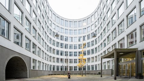 Innenhof mit geschwungenem, mehrstöckigem Bürogebäude, zwei Bäumen in der Mitte und zwei Personen im Gespräch
