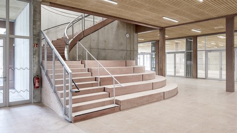 Moderner Innenraum mit geschwungener Treppe aus Beton und Holzdecke in einem hellen, offenen Gebäude