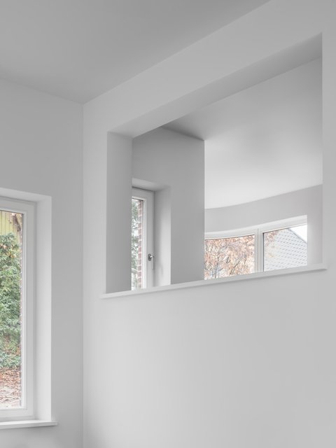 Blick durch eine große Wandöffnung auf helle Räume mit bodentiefen Fenstern und geschwungener Fensterfront.