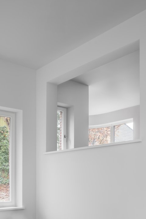 Blick durch eine große Wandöffnung auf helle Räume mit bodentiefen Fenstern und geschwungener Fensterfront.