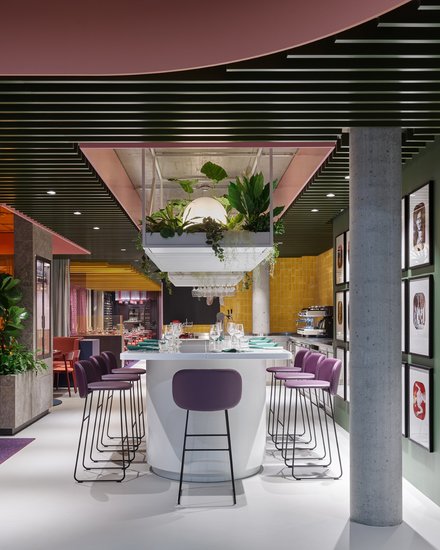 Farbintensives Restaurant mit Bar, Hockern, Pflanzen und hängender Beleuchtung.