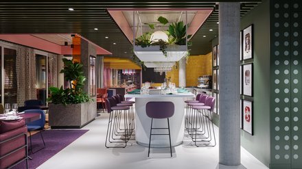 Farbintensives Restaurant mit Bar, Hockern, Pflanzen und hängender Beleuchtung.