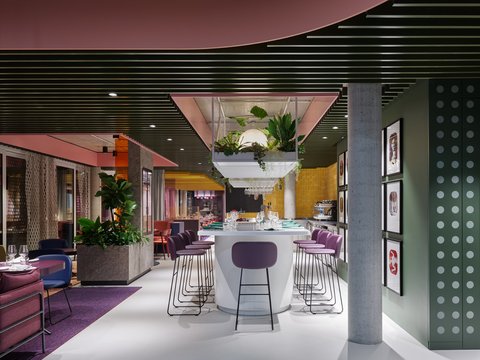 Farbintensives Restaurant mit Bar, Hockern, Pflanzen und hängender Beleuchtung.