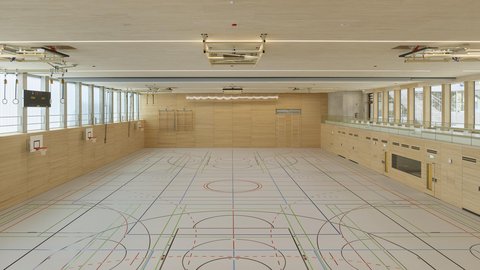 Leere Sporthalle mit Holzwänden, großen Fenstern und markiertem Spielfeldboden