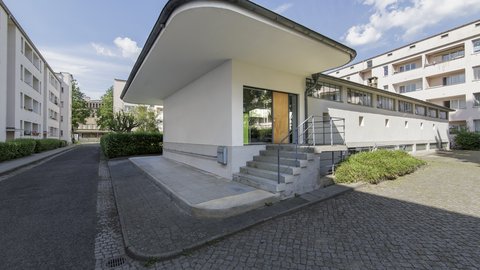 Modernisiertes Gebäude mit geschwungenem Dach und vorgelagerter Terrasse.