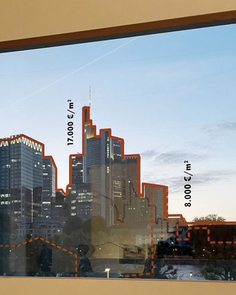 „Ein gerahmtes Bild einer Skyline an einer hellen Wand. Die Konturen der Wolkenkratzer sind im Foto mit roten Linien nachgezeichnet und mit vertikal angeordneten Maßangaben versehen.“