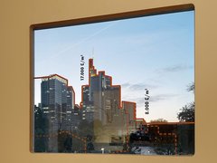 „Ein gerahmtes Bild einer Skyline an einer hellen Wand. Die Konturen der Wolkenkratzer sind im Foto mit roten Linien nachgezeichnet und mit vertikal angeordneten Maßangaben versehen.“
