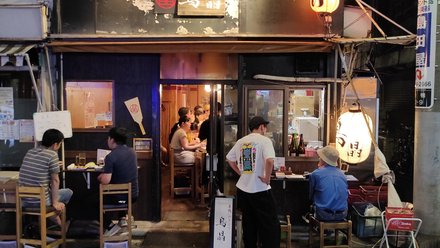 Kleines Straßenrestaurant bei Nacht mit Gästen an Tischen und leuchtenden Papierlaternen.