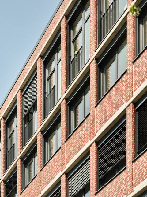 Fassade eines mehrstöckigen Backsteingebäudes mit mehreren Fenstern und schwarzen Jalousien