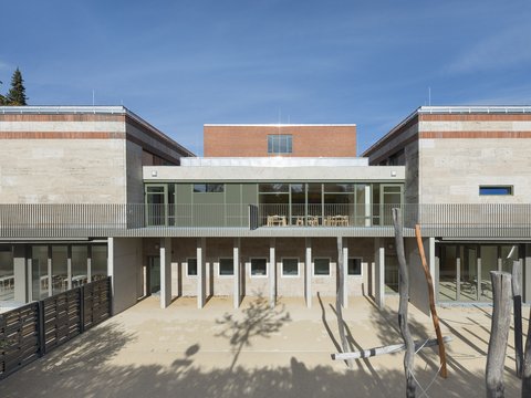 Moderner, zweigeschossiger Gebäudekomplex mit großflächigen Glasfronten und heller Fassade vor blauem Himmel