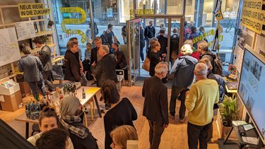 Gesprächsrunden im Innenraum einer Ausstellung mit Plakaten und Informationswänden.