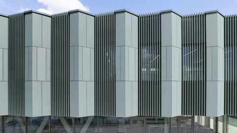 Fassade eines modernen Gebäudes mit vertikalen, unregelmäßig geformten Paneelen und großflächigen Fenstern im Erdgeschoss