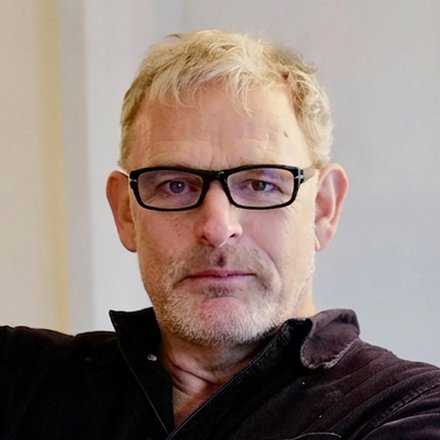 Porträt eines Mannes mit Brille vor einer neutralen Wand
