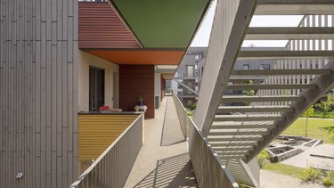 Blick auf farbige Fassaden und Treppen der Wohnanlage, mit hellen, begrünten Außenbereichen.