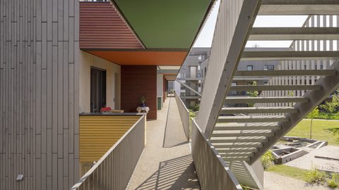 Blick auf farbige Fassaden und Treppen der Wohnanlage, mit hellen, begrünten Außenbereichen.