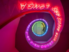 Bunte, spiralförmige Neonlichtinstallation mit lateinischem Text an einer Treppenhausdecke