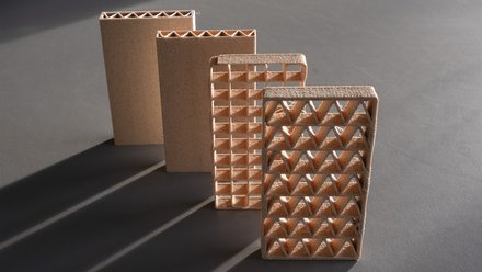 Vier 3D-gedruckte Lehmmodule mit unterschiedlichen inneren Gitterstrukturen stehen auf einer Oberfläche und zeigen verschiedene geometrische Stabilitätsmuster.