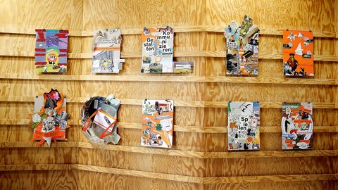 "Zwei Holzregale mit zehn verschiedenen farbigen Designmagazinen und Kunstpublikationen mit illustrierten Covern. Mehrere Magazine haben Pop-up- und 3D-Elemente. Überwiegend orange und rote Farbakzente auf hellem Sperrholz-Hintergrund."