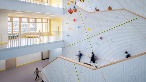 Helles, modernes Treppenhaus mit großen Fenstern, bunten Kugeln an der Decke und mehreren Personen auf den Treppen und im Gang