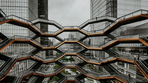  Große, wabenförmige Treppenanlage mit mehreren Ebenen zwischen hohen Glasgebäuden; wenige Personen auf den Stegen; urbanes Umfeld, bedeckter Himmel; Blick von innen nach außen.