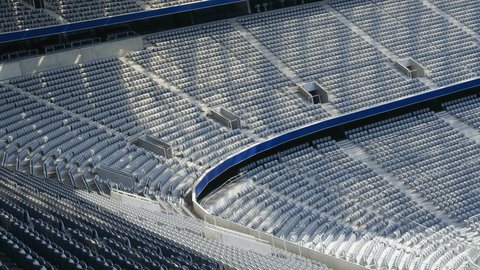 Leere Tribünen eines großen Fußballstadions mit weißen Kunststoffsitzen. Die Sitze sind in mehreren Ebenen angeordnet, verbunden durch Treppen und Korridore. Eine blaue Abschrankung trennt die Tribünenbereiche. Das Bild zeigt die massive Kapazität und Architektur eines modernen Stadions.
