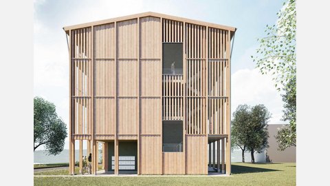 Stirnseite eines viergeschossigen Holzwohnhauses: vertikale Lamellen, Treppenhaus dahinter sichtbar; im Erdgeschoss offener Durchgang mit Briefkästen, Wiese und Bäume.