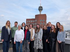 Gruppe von elf Personen auf einer Dachterrasse mit Turm und Stadthintergrund.