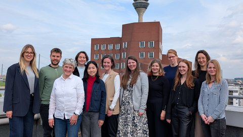 Gruppe von elf Personen auf einer Dachterrasse mit Turm und Stadthintergrund.