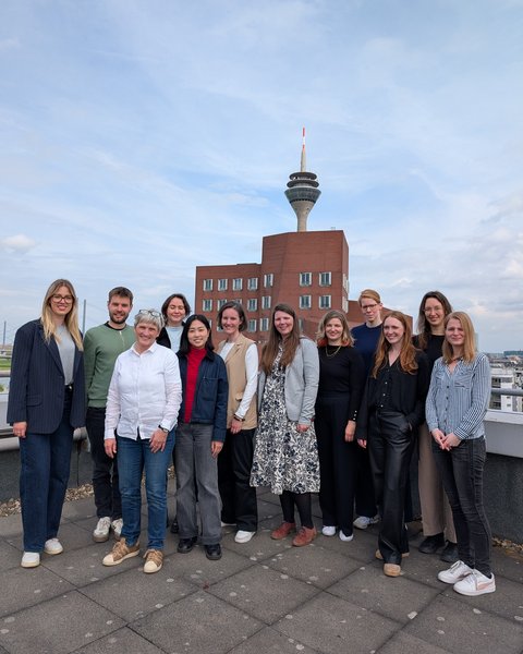 Gruppe von elf Personen auf einer Dachterrasse mit Turm und Stadthintergrund.
