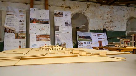 Detailaufnahme eines Architekturmodells auf einem Tisch, im Hintergrund hängen Entwurfspläne.