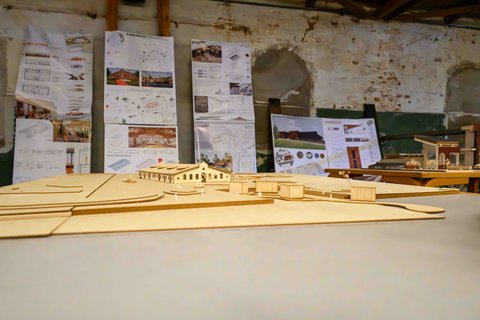 Detailaufnahme eines Architekturmodells auf einem Tisch, im Hintergrund hängen Entwurfspläne.