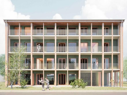 Frontansicht eines viergeschossigen Holzbaus mit grüner Fassade: durchgehende Balkone mit Netzgeländern hinter Holzstützen; mehrere Personen auf den Laubengängen, Bäume davor.