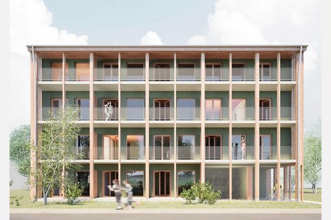 Frontansicht eines viergeschossigen Holzbaus mit grüner Fassade: durchgehende Balkone mit Netzgeländern hinter Holzstützen; mehrere Personen auf den Laubengängen, Bäume davor.