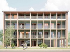 Frontansicht eines viergeschossigen Holzbaus mit grüner Fassade: durchgehende Balkone mit Netzgeländern hinter Holzstützen; mehrere Personen auf den Laubengängen, Bäume davor.