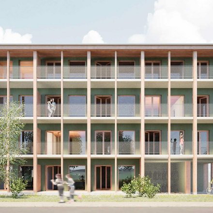 Frontansicht eines viergeschossigen Holzbaus mit grüner Fassade: durchgehende Balkone mit Netzgeländern hinter Holzstützen; mehrere Personen auf den Laubengängen, Bäume davor.