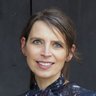 "Porträt einer lächelnden Frau mit zurückgebundenen Haaren. Sie trägt eine dunkelblaue Bluse mit Vogel- und Blumenmuster und steht vor einem dunkelgrauen Hintergrund."  Bild 3: Kochen im Freien
