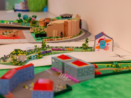 Mehrere kreative Architektur- und Stadtplanungsmodelle von Schülerinnen und Schülern auf einem Ausstellungstisch mit Gebäuden, Straßen und Grünflächen.