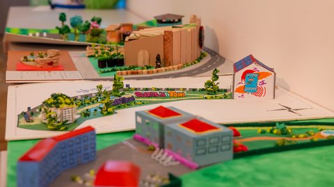 Mehrere kreative Architektur- und Stadtplanungsmodelle von Schülerinnen und Schülern auf einem Ausstellungstisch mit Gebäuden, Straßen und Grünflächen.