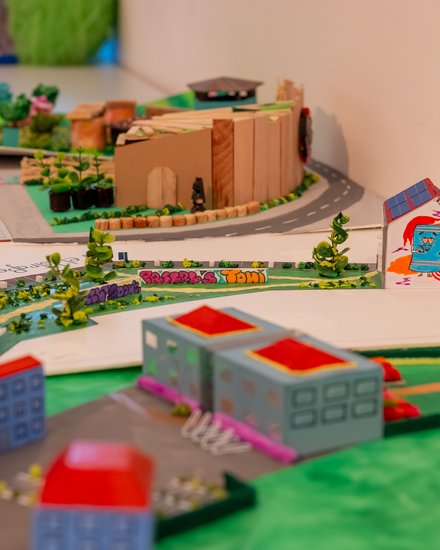Mehrere kreative Architektur- und Stadtplanungsmodelle von Schülerinnen und Schülern auf einem Ausstellungstisch mit Gebäuden, Straßen und Grünflächen.