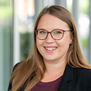 Porträt einer Frau mit Brille in Innenraum Freundlich lächelnde Frau im Business-Outfit vor hellem Hintergrund.