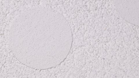 Weiße, grobkörnige Putzfläche mit runden, glatteren Ausbesserungsflecken.