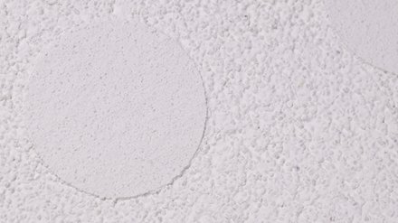 Weiße, grobkörnige Putzfläche mit runden, glatteren Ausbesserungsflecken.