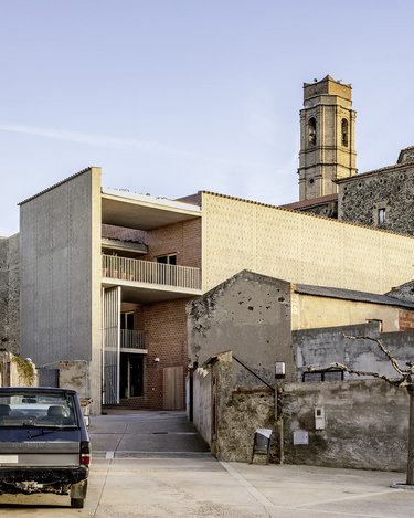 Historisches Steingebäude mit Kirchturm neben modernem, kubischem Neubau in ruhiger Hofsituation.
