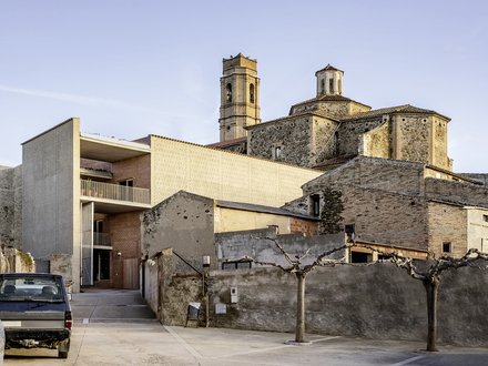 Historisches Steingebäude mit Kirchturm neben modernem, kubischem Neubau in ruhiger Hofsituation.