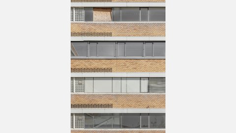 Detail einer Backsteinfassade  Ein enger Ausschnitt einer Gebäudefassade. Horizontale Backsteinbänder wechseln sich mit langen Fensterstreifen ab. Einige Fenster sind transparent, andere blickdicht oder provisorisch verschlossen. Die Fassade zeigt die serielle, funktionale Architektur des Gebäudes. Unterschiedliche Fensterzustände deuten auf Leerstand, Umbau oder wechselnde Nutzung hin.