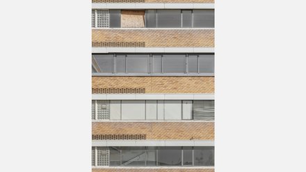 Detail einer Backsteinfassade  Ein enger Ausschnitt einer Gebäudefassade. Horizontale Backsteinbänder wechseln sich mit langen Fensterstreifen ab. Einige Fenster sind transparent, andere blickdicht oder provisorisch verschlossen. Die Fassade zeigt die serielle, funktionale Architektur des Gebäudes. Unterschiedliche Fensterzustände deuten auf Leerstand, Umbau oder wechselnde Nutzung hin.