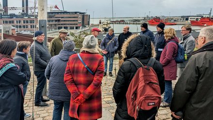 Gruppe von Menschen hört einer Führung mit Blick auf einen Hafen zu.