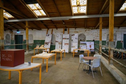 Innenraum einer alten Halle mit Ausstellungstischen, Architekturplänen und Modellen.