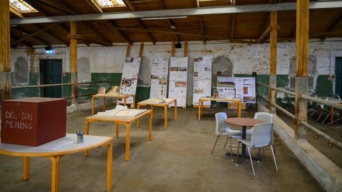 Innenraum einer alten Halle mit Ausstellungstischen, Architekturplänen und Modellen.