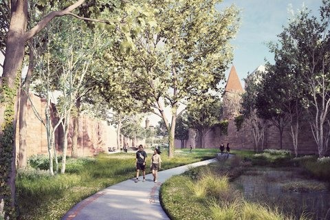 Schmaler gepflasterter Fußweg mit rotem Ziegelbelag entlang eines flachen Wasserlaufs. Hohe Bäume säumen beide Seiten. Paare joggen/gehen auf dem Weg. Historische Steinmauern und Gebäudetürme sichtbar. Grüne Vegetation und Wiese.